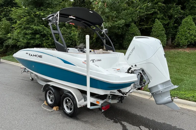 Slide: The Image of 2026 Tahoe 2150 boat on trailer with Mercury outboard motor, parked near lush greenery. - 6