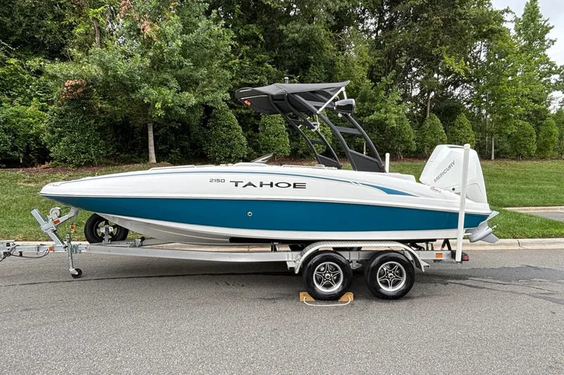 The Image of 2026 Tahoe 2150 boat on trailer, parked on road with lush greenery background. - 0