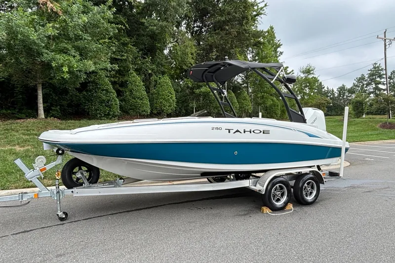 Slide: The Image of 2026 Tahoe 2150 boat on trailer, parked outdoors with lush greenery background. - 1