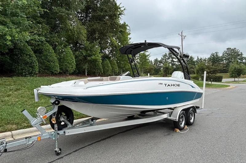 Slide: The Image of 2026 Tahoe 2150 boat on trailer, parked outdoors, surrounded by greenery and overcast sky. - 2
