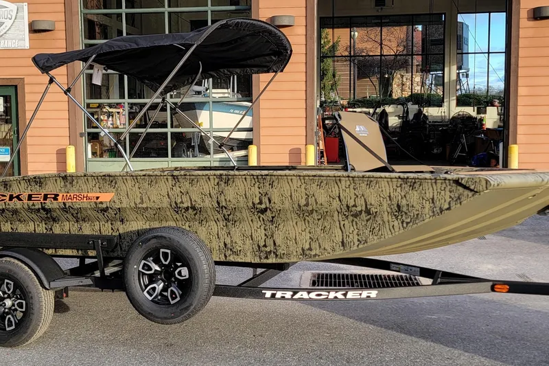 The Image of 2026 Tracker Grizzly 1756 T Marsh boat with canopy on trailer, parked outside a building. - 0