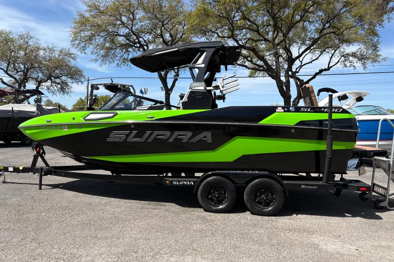 Slide: The Image of 2023 Supra SL 400 boat in vibrant green and black on a trailer, parked outdoors. - 24