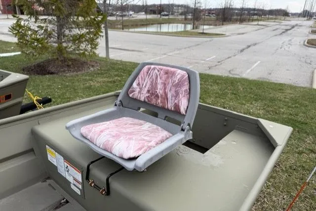 Slide: The Image of 2024 Tracker Grizzly 1436 Jon boat with a pink camo seat in a parking area. - 3
