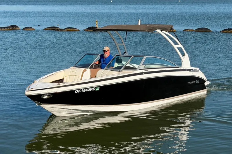 Slide: The Image of 2013 Cobalt 232 boat cruising on a calm lake with a person at the helm. - 2