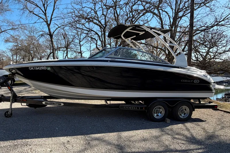 Slide: The Image of 2013 Cobalt 232 boat on trailer, parked outdoors with trees in the background. - 6