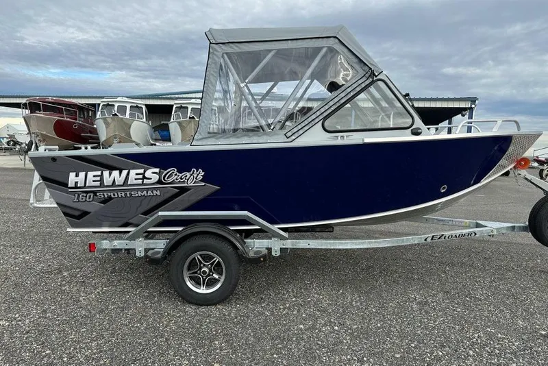 The Image of 2026 Hewescraft 160 Sportsman boat on trailer, featuring a sleek blue design. - 7
