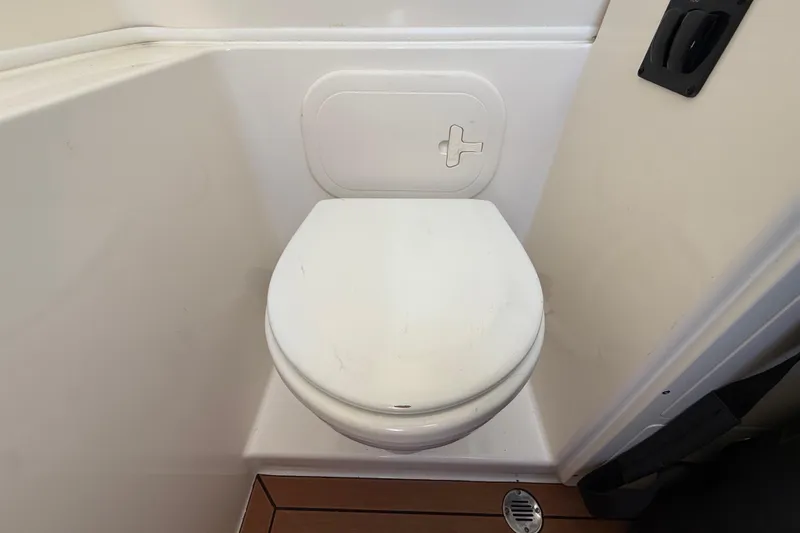 Slide: The Image of Toilet in 2017 Cobia 296 Center Console boat, featuring white seat and wooden flooring. - 27