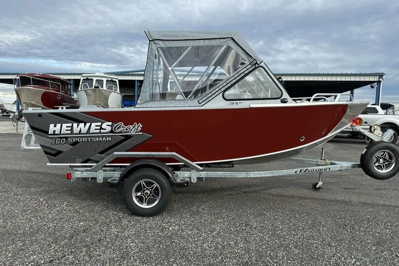 The Image of 2026 Hewescraft 160 Sportsman boat on trailer, red exterior, parked outdoors. - 0