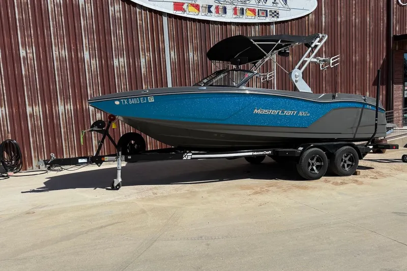 Slide: The Image of 2018 MasterCraft NXT22 boat on trailer, parked outdoors, with blue and gray design. - 1