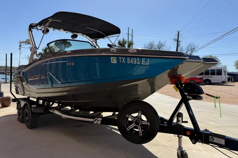 Slide: The Image of 2018 MasterCraft NXT22 boat on trailer, blue hull, parked outdoors. - 2