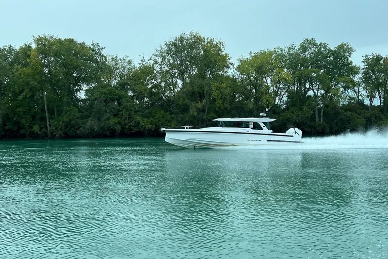 Slide: The Image of 2027 Axopar 38 Cross Cabin cruising on a serene lake with lush green trees. - 1
