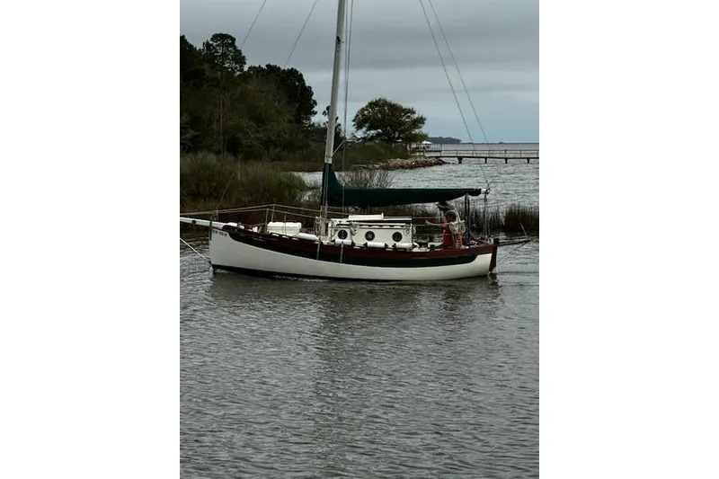 Slide: The Image of 1982 Falmouth Cutter 22 sailboat anchored on a calm river with overcast skies. - 15