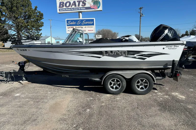 The Image of 2015 Lund 1900 Tyee boat on trailer, parked outdoors near sales and service sign. - 1
