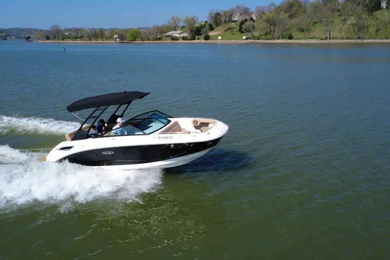 Slide: The Image of 2023 Sea Ray SDX 250 cruising on a serene lake with lush green shoreline. - 13