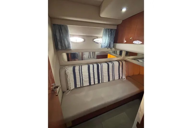 Slide: The Image of 1999 Sea Ray 480 Sedan Bridge cabin interior with bed, striped blanket, and porthole windows. - 63