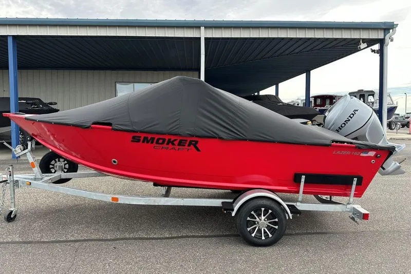 Slide: The Image of 2026 Smoker Craft Lazer 162 boat, red with cover, on trailer, parked outdoors. - 3