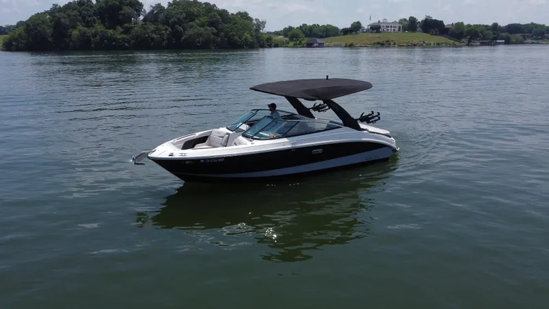 Slide: The Image of 2023 Sea Ray SLX 260 Surf boat on calm lake with lush green shoreline. - 2