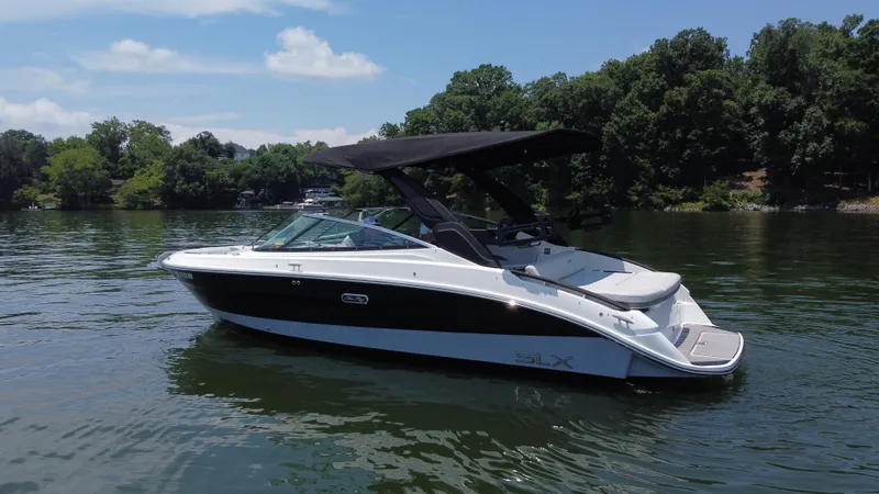 Slide: The Image of 2023 Sea Ray SLX 260 Surf boat on a calm lake with lush green trees. - 3