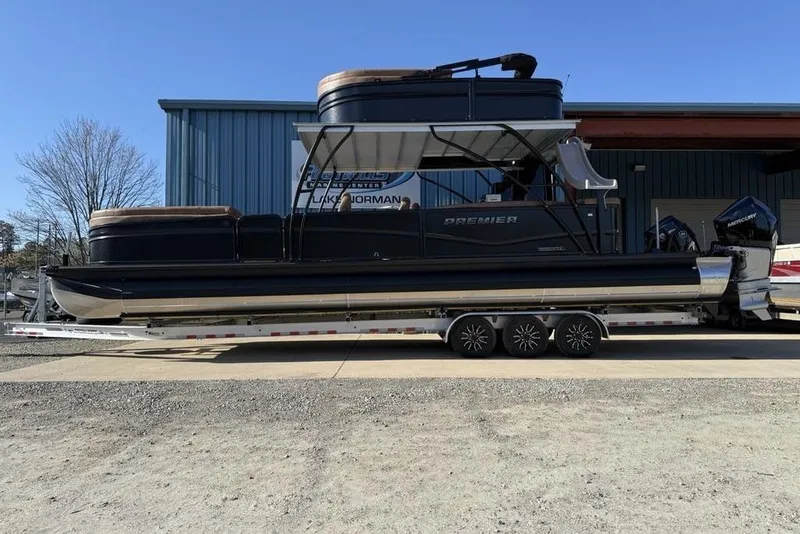 The Image of 2026 Premier 330 Escalante pontoon boat on trailer, parked outside a blue building. - 1