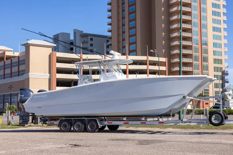 Slide: The Image of 2014 Freeman 33 boat on trailer, parked near tall buildings under clear blue sky. - 13