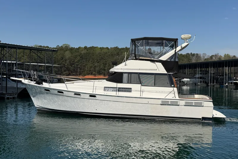 Slide: The Image of 1994 Bayliner 3888 MY Sedan yacht docked on a serene lake under clear skies. - 13