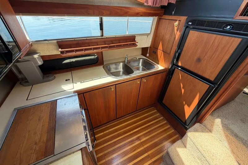 Slide: The Image of 1994 Bayliner 3888 MY Sedan kitchen with wood cabinetry, dual sink, and refrigerator. - 34
