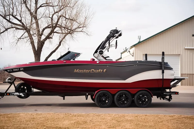 The Image of 2019 MasterCraft X24 boat on trailer, parked near a building, showcasing sleek design. - 0