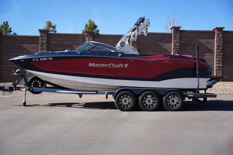 The Image of 2019 MasterCraft X24 boat on trailer, red and blue design, parked outdoors. - 1