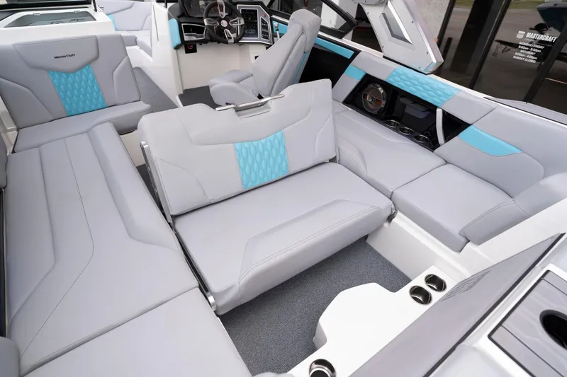 Slide: The Image of 2022 MasterCraft XT22 boat interior with gray and blue seating, modern dashboard, and cup holders. - 13