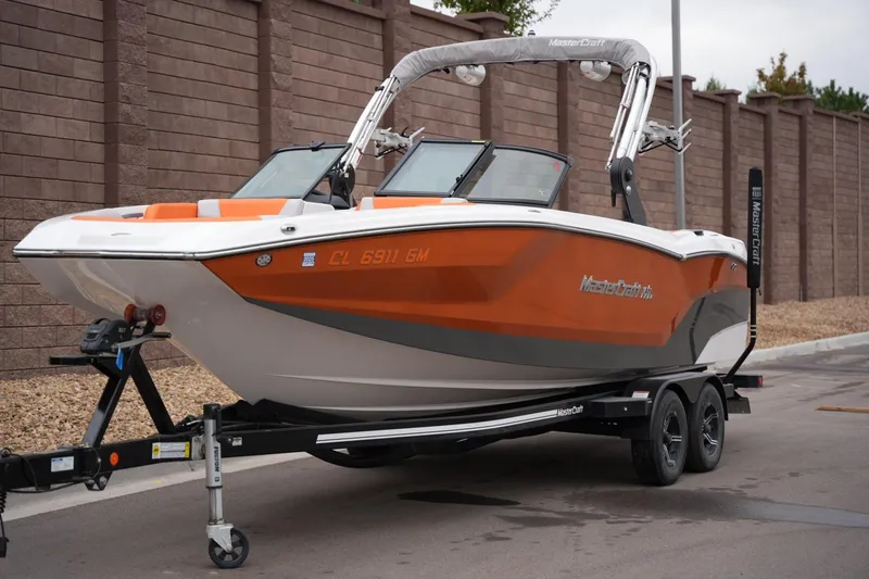 Slide: The Image of 2021 MasterCraft NXT24 boat on trailer, orange and white design, parked on street. - 8