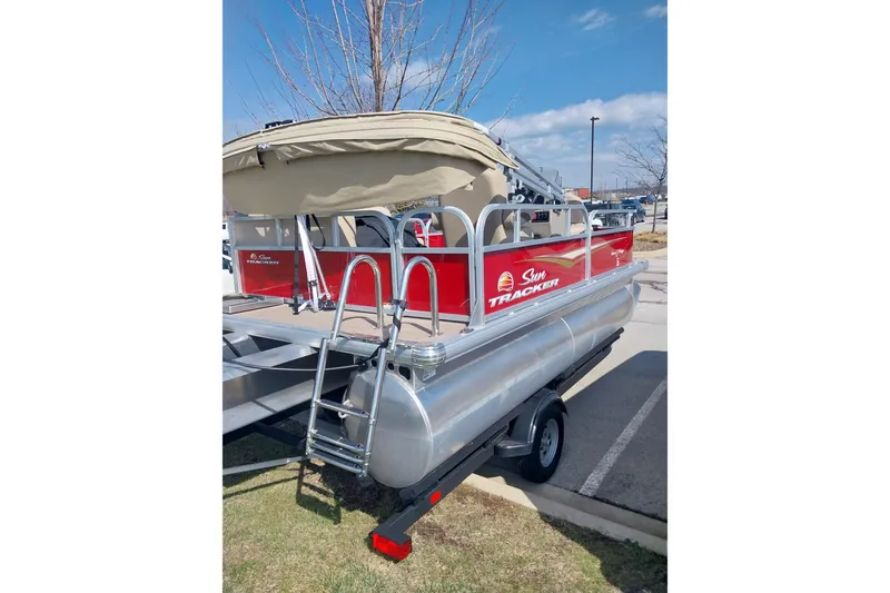 Slide: The Image of 2025 Sun Tracker Bass Buggy 16 DLX pontoon boat with canopy and ladder, parked outdoors. - 7