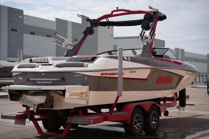 Slide: The Image of 2022 Malibu Wakesetter 23 MXZ boat on trailer, parked outdoors near industrial buildings. - 4
