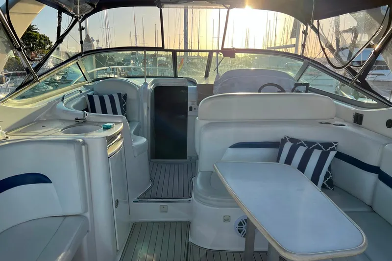 Slide: The Image of 2003 Chaparral Signature 320 boat interior with seating, table, and striped cushions at sunset. - 10