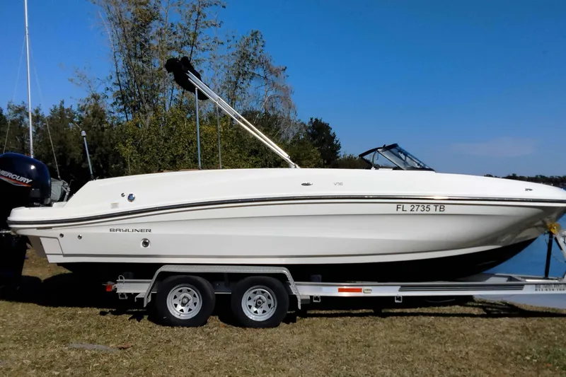 The Image of 2022 Bayliner VR6 Bowrider OB on trailer, parked near water and trees. - 1