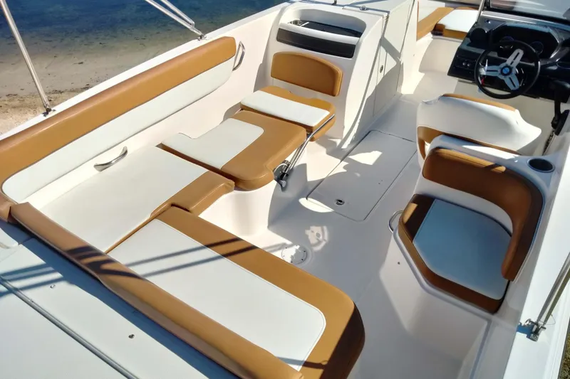 Slide: The Image of 2022 Bayliner VR6 Bowrider OB interior with tan and white seating, near sandy shore. - 12