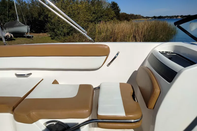 Slide: The Image of 2022 Bayliner VR6 Bowrider OB interior with tan and white seating by a lake. - 18