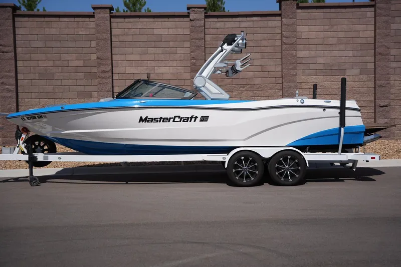 The Image of 2021 MasterCraft XT25 boat on trailer, parked against brick wall. - 1