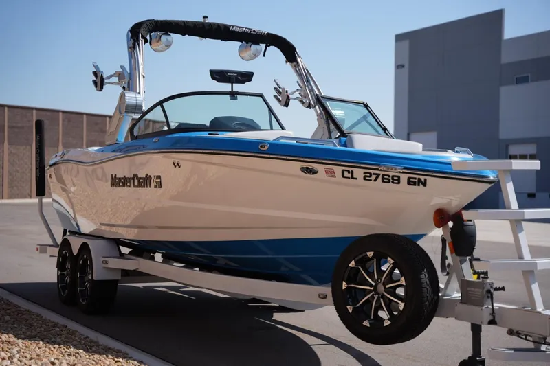 Slide: The Image of 2021 MasterCraft XT25 boat on trailer, blue and white design, parked outdoors. - 5