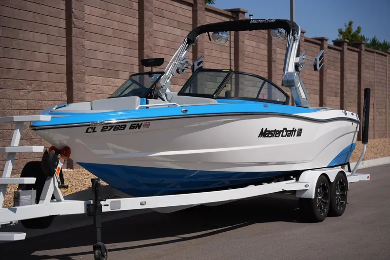 Slide: The Image of 2021 MasterCraft XT25 boat on trailer, blue and white design, parked outdoors. - 7