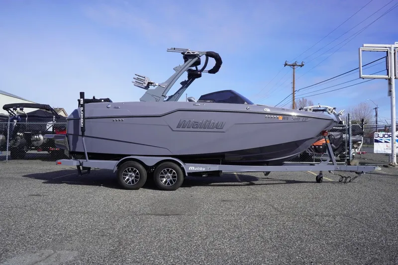 The Image of 2023 Malibu M220 boat on trailer, parked outdoors, side view. - 1