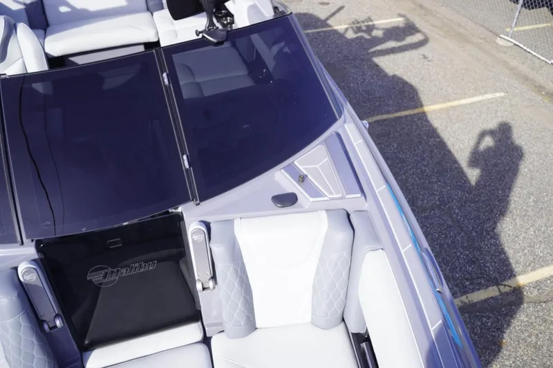 Slide: The Image of 2023 Malibu M220 boat interior with sleek seating and windshield, parked on pavement. - 42
