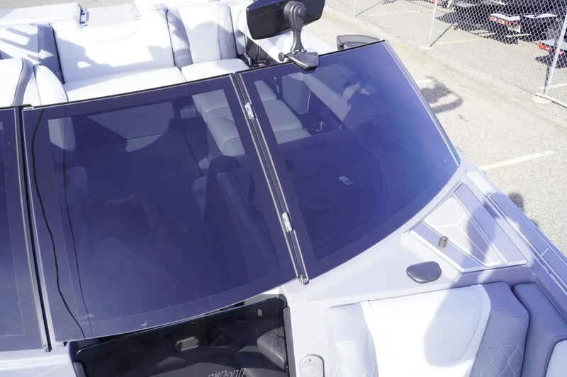 Slide: The Image of 2023 Malibu M220 boat interior with windshield and seating, parked near a fence. - 46