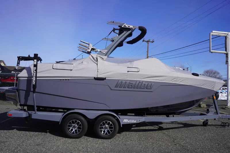 Slide: The Image of 2023 Malibu M220 boat covered on trailer, parked outdoors. - 52