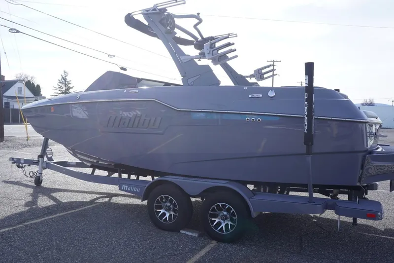Slide: The Image of 2023 Malibu M220 boat on trailer, parked outdoors, side view. - 8