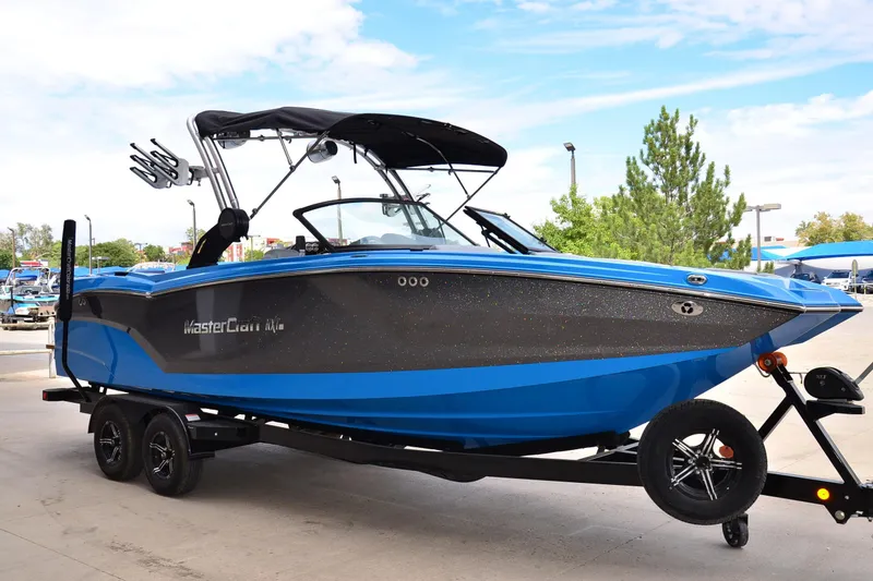 Slide: The Image of 2022 MasterCraft NXT24 boat in blue and black on a trailer, outdoors. - 5