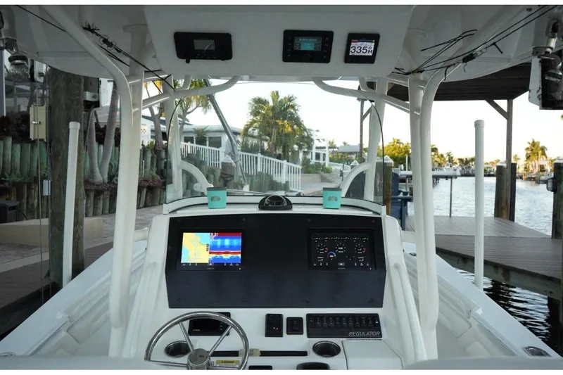 Slide: The Image of 2018 Regulator 28 boat dashboard with navigation screens and steering wheel, docked by waterfront homes. - 18