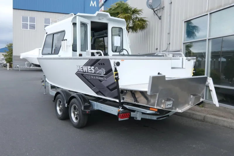Slide: The Image of 2026 Hewescraft 210 Sea Runner ET Hardtop boat on trailer, parked outside a building. - 4