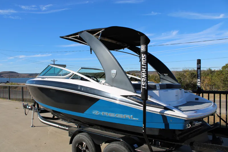 Slide: The Image of 2017 Regal 2100 Bowrider boat on trailer, blue and white design, outdoor setting. - 4