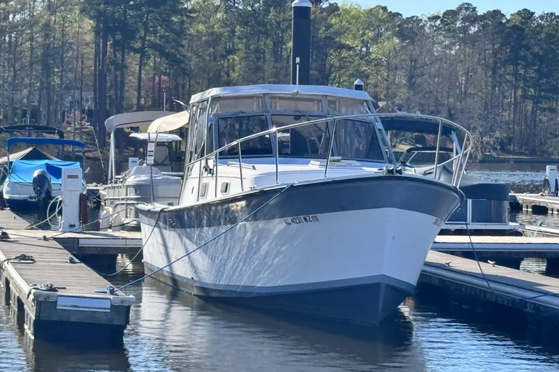 The Image of 1987 Luhrs Alura 30 boat docked at a marina, surrounded by trees. - 0