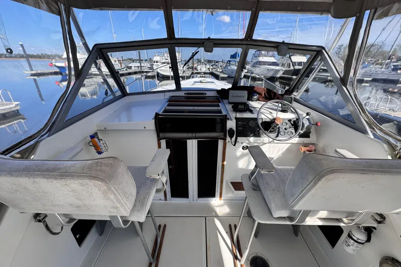 Slide: The Image of 1987 Luhrs Alura 30 boat cockpit with steering wheel, seats, and marina view. - 11